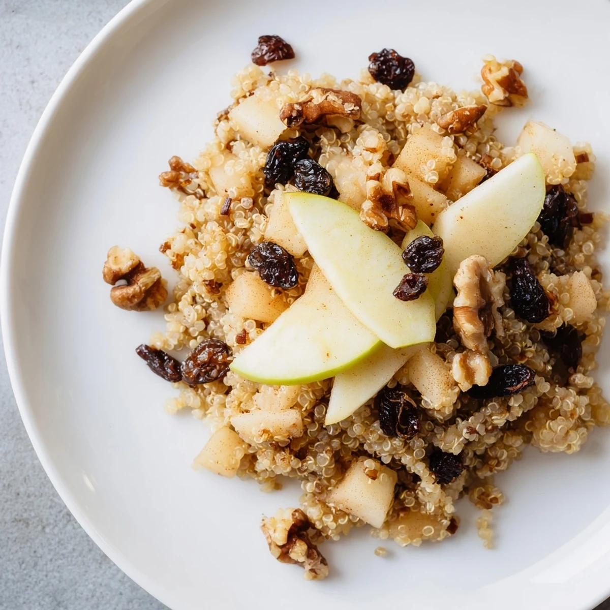 Steaming apple cinnamon quinoa bowl, speckled with nuts and raisins, ready for a warm breakfast.