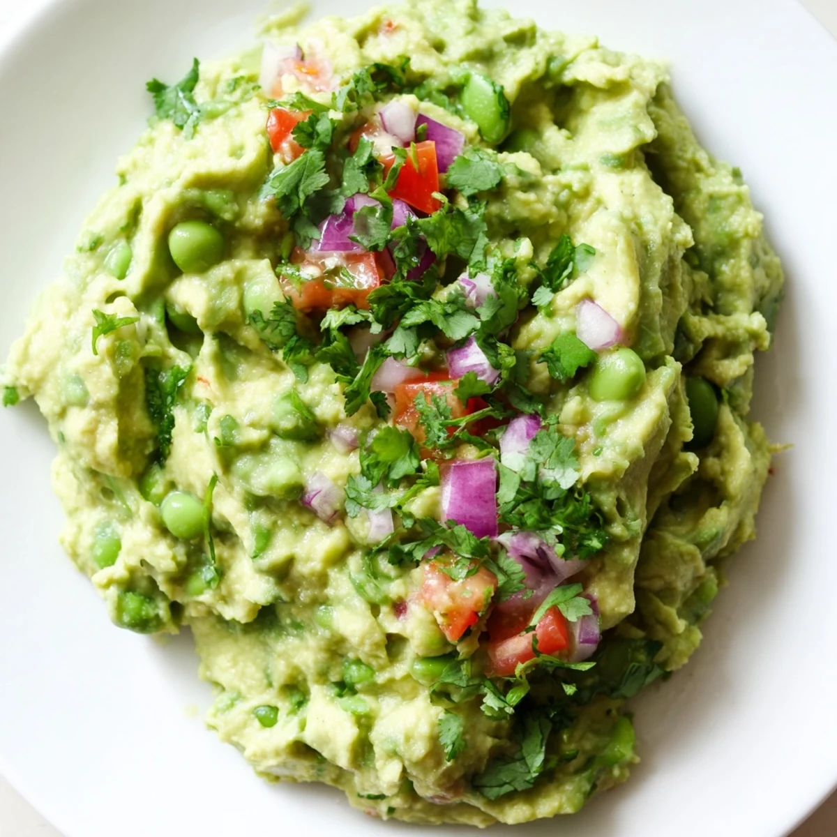 Creamy edamame guacamole served in a bowl, speckled with colorful tomatoes and red onion.