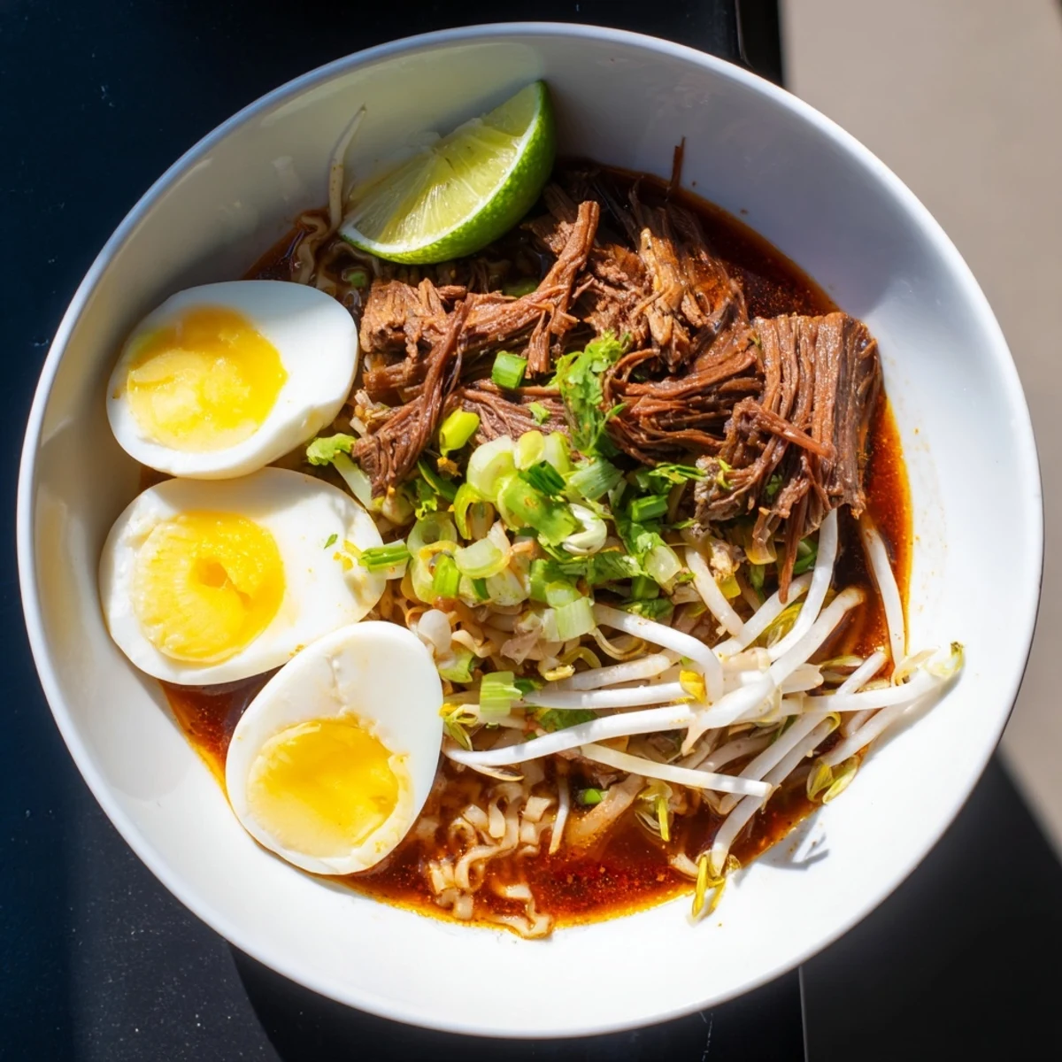 A close up showcases the rich, flavorful birria ramen broth with tender shredded beef and noodles.