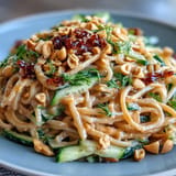 A refreshing serving of cold peanut sesame noodles, topped with crunchy peanuts, scallions, and cucumber.