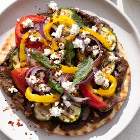 A close-up of a warm naan bread pizza featuring olive tapenade, feta, and fresh basil.