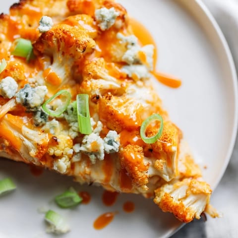 A golden Buffalo Cauliflower Pizza slice topped with celery and blue cheese crumbles, served on a wooden cutting board for a rustic look.  