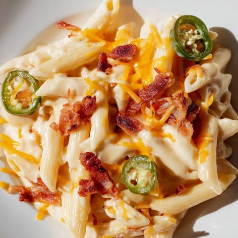 A close-up of cheesy Jalapeño Popper Pasta twirled on a fork, showcasing its rich texture and spicy green garnish.