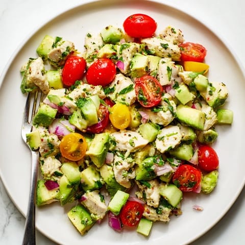 Fresh avocado chicken salad served with juicy tomatoes and cucumber, garnished with bright cilantro and lime.  