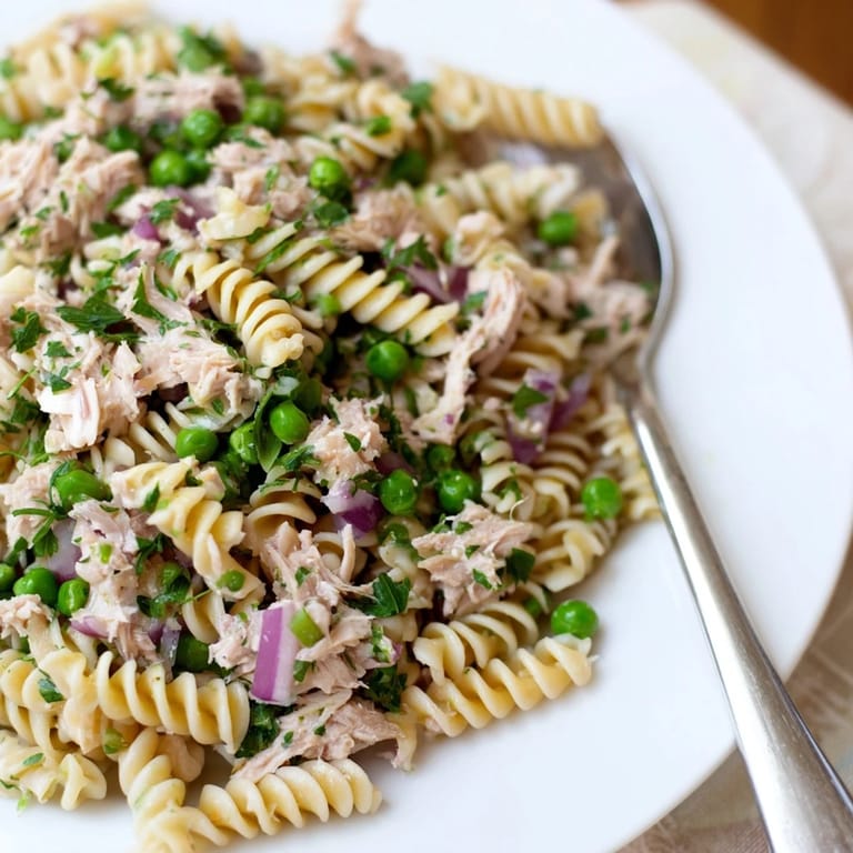 Close-up of Lemony Tuna Pasta Salad featuring fusilli pasta, tender tuna chunks, and finely diced red onion glistening with olive oil.